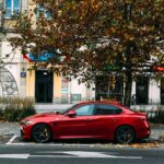 A sleek red sports car parked on a city street lined with autumn trees.